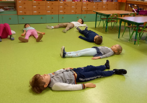 Dzieci leżą na podłodze na plecach i odpoczywają po ćwiczeniach.